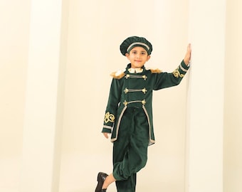 May include: A dark green velvet child's costume, comprising a jacket, trousers, and hat. The jacket has gold trim, buttons, and embroidered sleeve details. The outfit is finished with black shoes and a white collar.