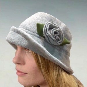 May include: A light gray fleece hat with a large gray fabric rose and green leaf embellishment.