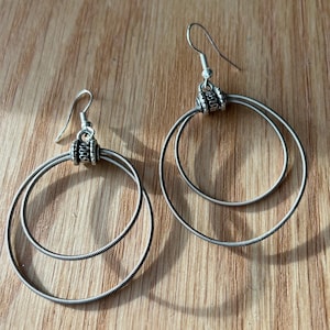 May include: A pair of silver hoop earrings made from guitar strings. The earrings are double-layered and have a decorative bead at the top.