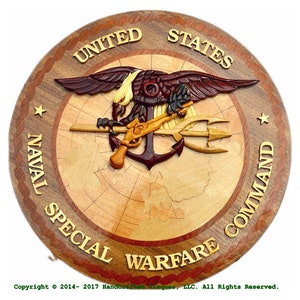 May include: A wooden plaque featuring the United States Naval Special Warfare Command emblem. The emblem includes an eagle, anchor, trident, and a gun, all in various shades of brown and tan. The text "UNITED STATES NAVAL SPECIAL WARFARE COMMAND" is carved around the edge.