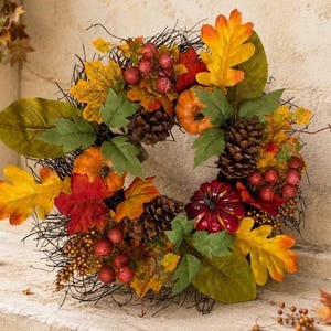 May include: A decorative wreath featuring a dark twig base adorned with artificial autumn elements including orange and deep red pumpkins, brown pinecones, clusters of red berries, and vibrant yellow, orange, and green maple and oak leaves.