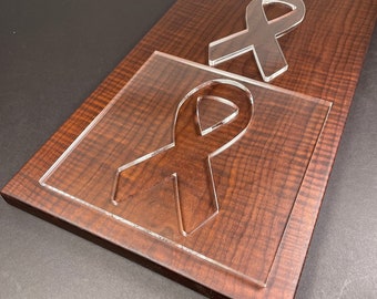 May include: Two clear acrylic squares with a ribbon design cut out. The squares are on a dark brown wooden surface.