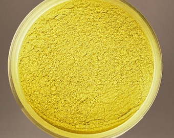 May include: A close-up of a small, round container filled with a bright yellow powder. The powder has a fine, granular texture.