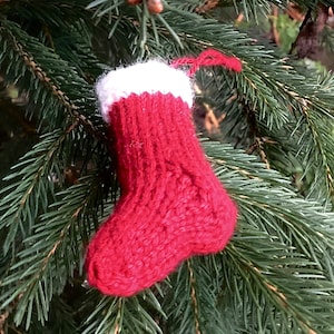 May include: A red knitted stocking with a white cuff, hanging on a green pine tree branch.