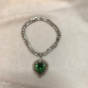 May include: A silver necklace with a double row of clear rhinestones and a green heart-shaped pendant.
