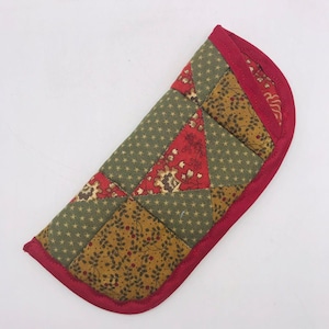 May include: A red and green patchwork fabric glasses case with a red border.