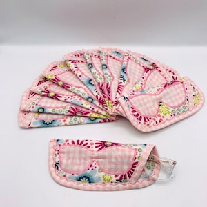 May include: A stack of pink and white gingham fabric eyeglass cases with floral embroidery. The cases are folded in a fan shape and have a scalloped edge.