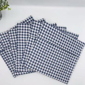 Può includere: Sono presentati cinque tovagliette a scacchi blu navy e bianche. Le tovagliette quadrate sono realizzate in tessuto. Il motivo a scacchi presenta quadrati blu navy e bianchi distanziati uniformemente. Le tovagliette sono ben disposte, suggerendo che siano nuove o inutilizzate.