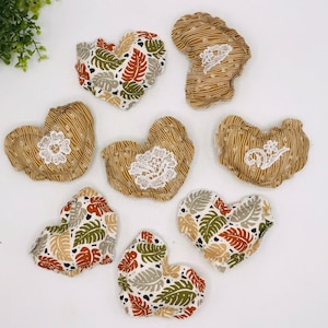 May include: A collection of heart-shaped fabric ornaments. Some hearts feature a brown and white striped pattern with white lace accents. Others display a tropical leaf print in shades of green, brown, and gray.