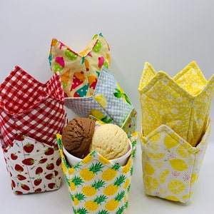 May include: Five fabric ice cream cup holders in various patterns. The holders are in the shape of a crown. The patterns include red and white gingham, strawberries, pineapples, lemons, and ice cream cones.