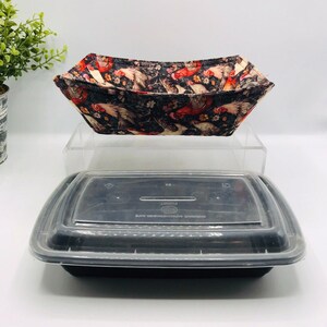 Puede incluir: Un cuenco de tela con un diseño de gallo negro y rojo se encuentra encima de un recipiente rectangular negro para alimentos con una tapa transparente. El cuenco está abierto e inclinado, mostrando el patrón de gallo y floral.