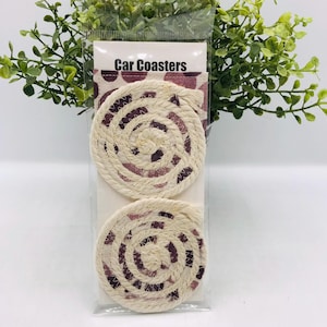 May include: Two car coasters in a clear plastic package. The coasters are made of cream-colored rope in a spiral design, with a burgundy and cream fabric center. The packaging has the words "Car Coasters" printed on it.