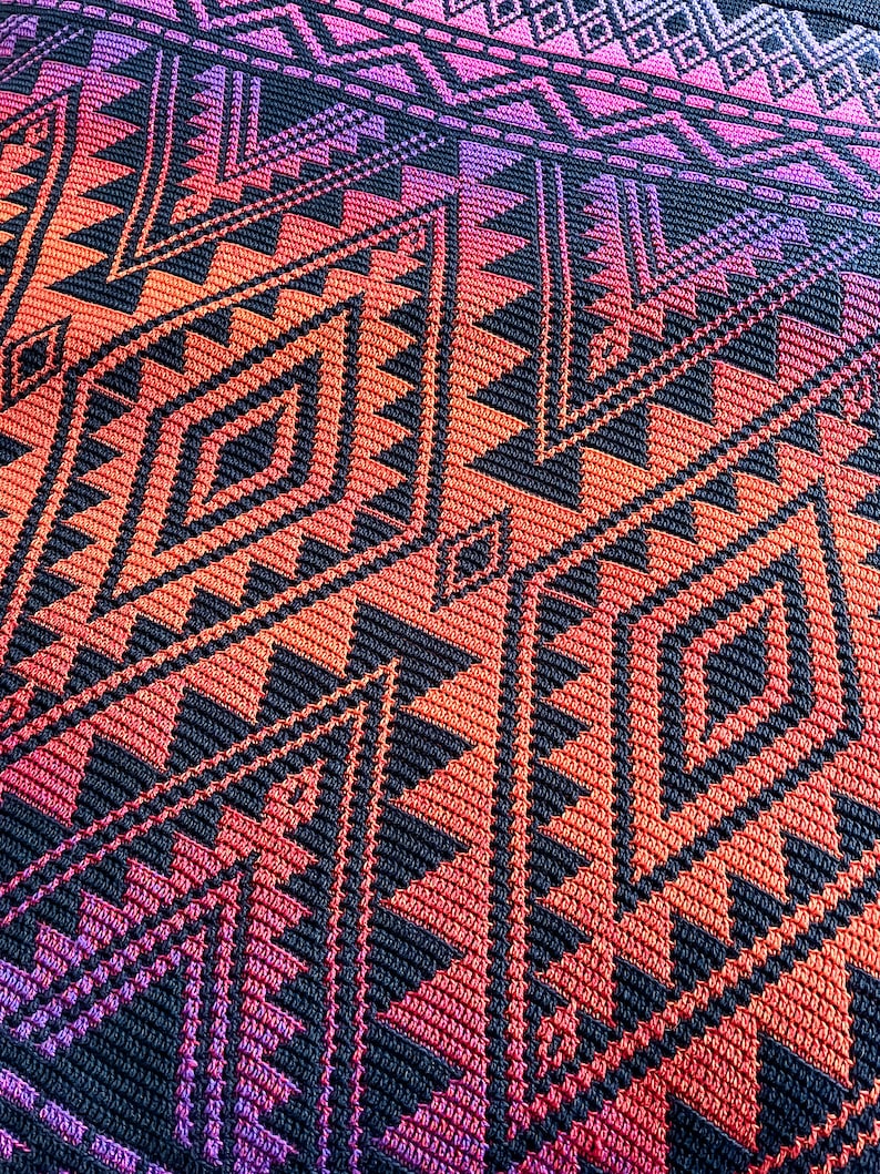 May include: A close-up of a crocheted blanket with a geometric pattern in shades of pink, orange, and black.