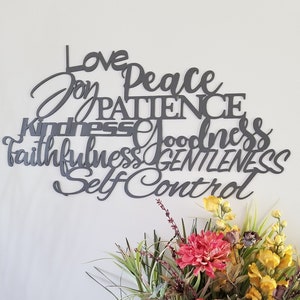 The words love joy peace patience kindness goodness faithfulness gentleness and self control are displayed in two different fonts, printed and cursive, upper and lower case lettering and connected together to hang on the wall as a single piece.