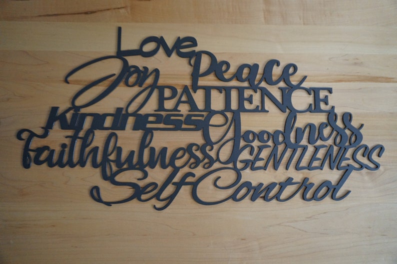 The words love joy peace patience kindness goodness faithfulness gentleness and self control are displayed in two different fonts, printed and cursive, upper and lower case lettering and connected together to hang on the wall as a single piece.