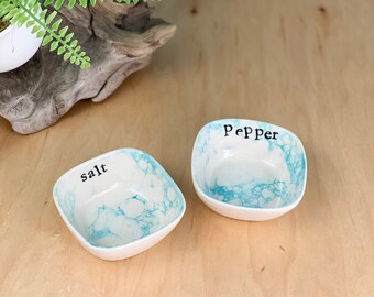 May include: Two small, square ceramic salt and pepper shakers with a blue and white marbled design. The salt shaker says "salt" and the pepper shaker says "pepper".
