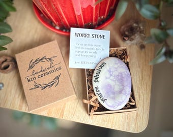 May include: A small, purple and white worry stone with the text "You're fabulous" written on it. The stone is in a small box with a card that reads "Worry Stone" and "Just keep going".