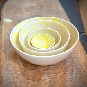 May include: Set of four nesting bowls with a white base and yellow marbling. The bowls are arranged in size order, with the largest bowl on the bottom and the smallest bowl on top.