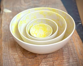 May include: Set of four nesting bowls with a white base and yellow marbling. The bowls are arranged in size order, with the largest bowl on the bottom and the smallest bowl on top.