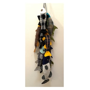 May include: A group of handmade fabric fish toys hanging from a string. The fish are made from different patterned fabrics, including plaid, striped, and solid colors. The fish have yellow, blue, and green accents.