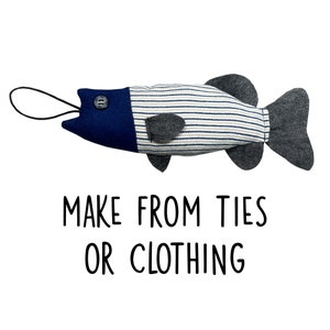 May include: A blue and white striped fabric fish with a blue felt head and a black button for an eye. The fish has a gray felt tail fin and a black cord for a mouth. The text "MAKE FROM TIES OR CLOTHING" is printed below the fish.