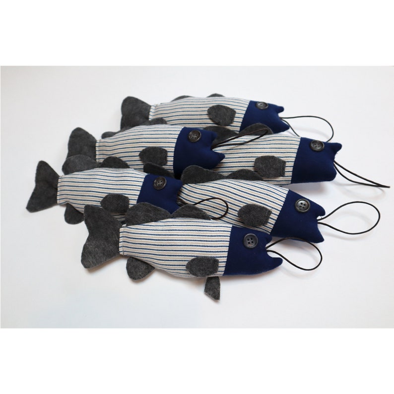 May include: Five plush toy fish with blue and white striped fabric, gray felt fins, and black button eyes. The fish are hanging from black cords.