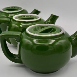 Peut inclure: Trois théières en céramique verte avec des couvercles blancs. Les théières sont toutes de la même taille et de la même forme, et elles ont un design classique.