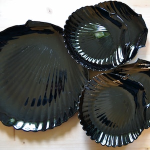 May include: Three black glass serving dishes shaped like seashells. The dishes are nested together, with the largest dish at the bottom and the smallest dish at the top.