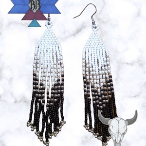 May include: A pair of long, beaded earrings with a gradient of white, silver, and black beads. The earrings are hanging from silver hooks.