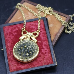 May include: A gold necklace with a round pendant featuring a floral design and the word "Mum". The pendant is attached to a bow and the necklace is in a red velvet box.