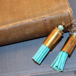 May include: A pair of turquoise tassel earrings made with bullet casings and turquoise beads. The earrings are hanging from a book.