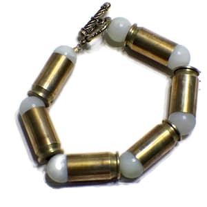 May include: A bracelet made of brass bullet casings and white beads. The bracelet has a clasp made of metal.