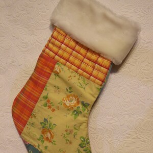 May include: A patchwork Christmas stocking with a white faux fur cuff. The stocking is made of different fabrics with floral and plaid patterns in shades of yellow, orange, red, and blue.