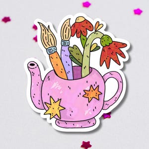 Puede incluir: Una pegatina caprichosa con una tetera rosa con detalles de estrellas amarillas. La tetera contiene dos pinceles y flores coloridas con pétalos rojos y verdes. La pegatina tiene un borde blanco y está rodeada de confeti de estrellas rosas.