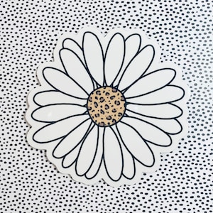 Puede incluir: Una margarita blanca con un contorno negro y un centro de estampado de leopardo. La margarita está sobre un fondo de lunares negros y blancos.