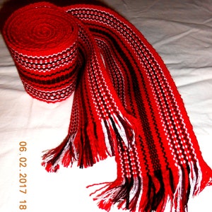 May include: A red, white, and black woven belt with fringe. The belt is rolled up and tied in a knot.