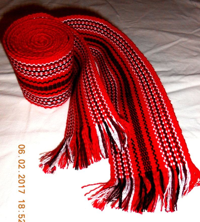 May include: A red, white, and black woven belt with fringe. The belt is rolled up and tied in a knot.