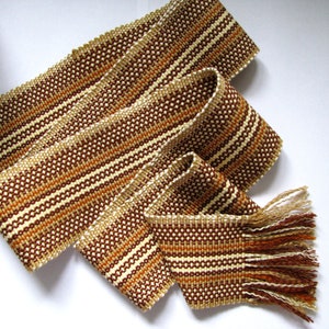 May include: A woven brown, white, and orange belt with a fringe on one end.