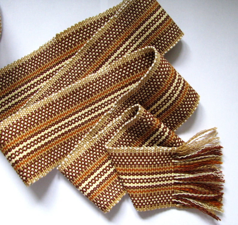 May include: A woven brown, white, and orange belt with a fringe on one end.