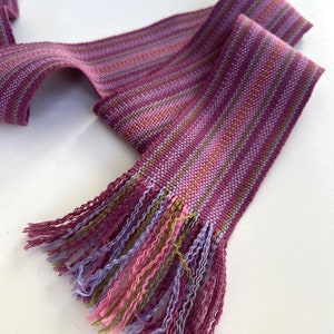 May include: A purple, pink, and green striped woven ribbon with a fringe on one end.