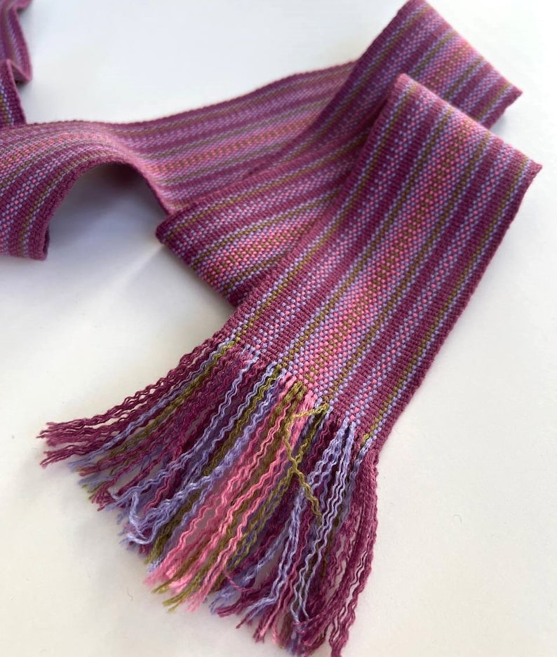 May include: A purple, pink, and green striped woven ribbon with a fringe on one end.