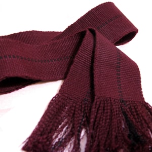 May include: A maroon fabric sash with black stripes and a fringe on the end.