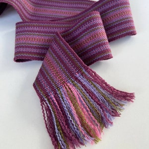 May include: A woven purple, pink, and green striped ribbon with a fringe on one end.