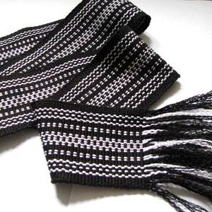 Könnte beinhalten: Schwarz-weißes gewebtes Band mit Fransen. Das Band hat ein geometrisches Muster aus weißen Punkten auf schwarzem Hintergrund.