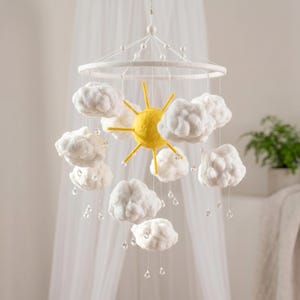 May include: A hanging mobile featuring a central yellow sun with radiating rays surrounded by multiple white fluffy clouds. Clear, teardrop-shaped beads hang from the clouds on thin strings, simulating falling rain droplets from the sky.