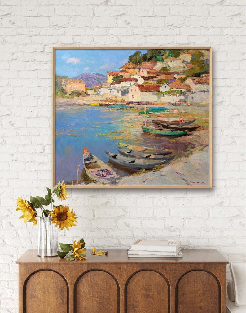 May include: A painting of a small village on a hillside with boats in the water. The sky is blue and the water is a light blue. The boats are various shades of green and brown. The village is painted in shades of yellow, orange, and red.