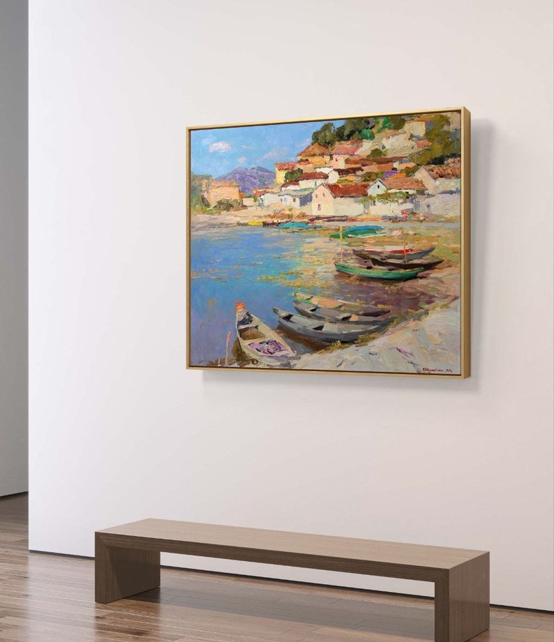 May include: A painting of a small village on a hillside overlooking a body of water with several boats docked. The water is a light blue color and the sky is a bright blue with white clouds. The village is painted in shades of pink, yellow, and brown.
