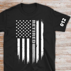 May include: Black t-shirt with a white distressed American flag design and the word "RETIRED" printed vertically on the flag. The number "012" is printed on the right sleeve.