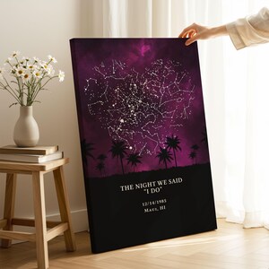 A person's hand is holding up a canvas print of a starry night sky with palm trees in the background.