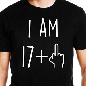 May include: Black t-shirt with white text that reads "I AM 17 +" and a white middle finger graphic.